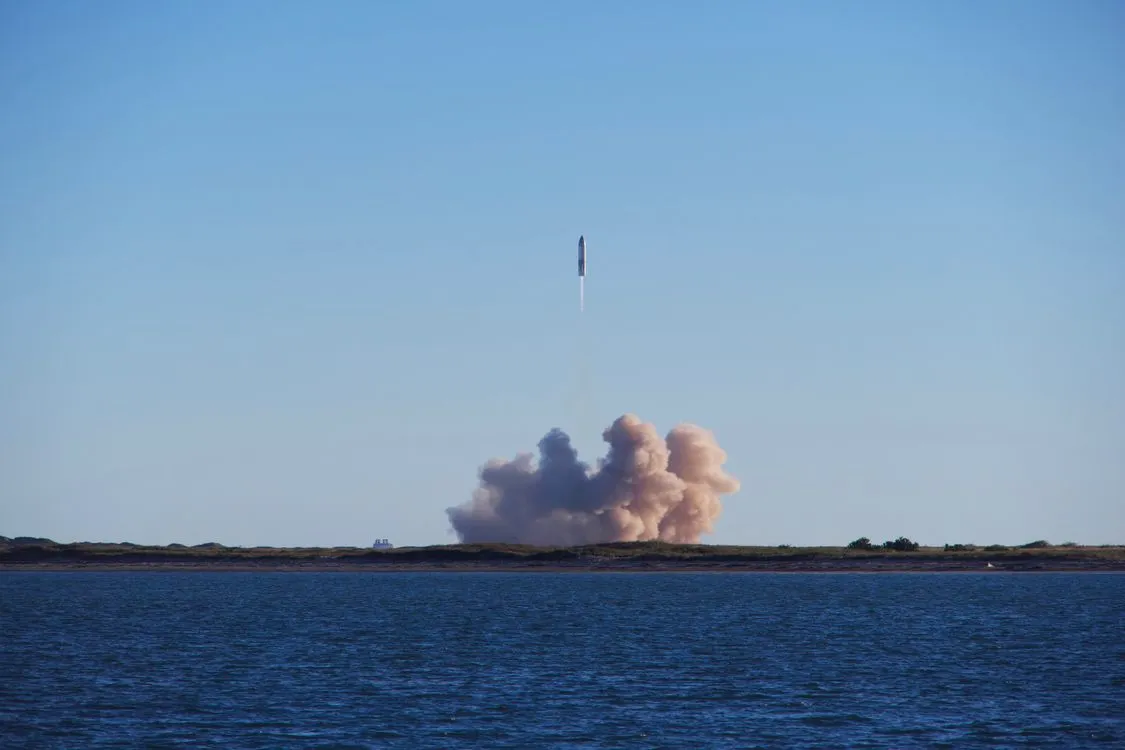 A rocket lifting off the launch pad with a bright exhaust plume against a clear sky.